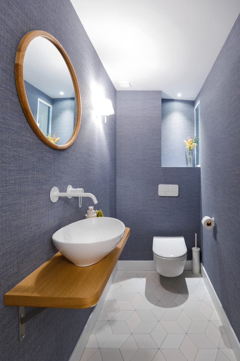 Aseo con pared azul, espejo redondo y repisa de madera