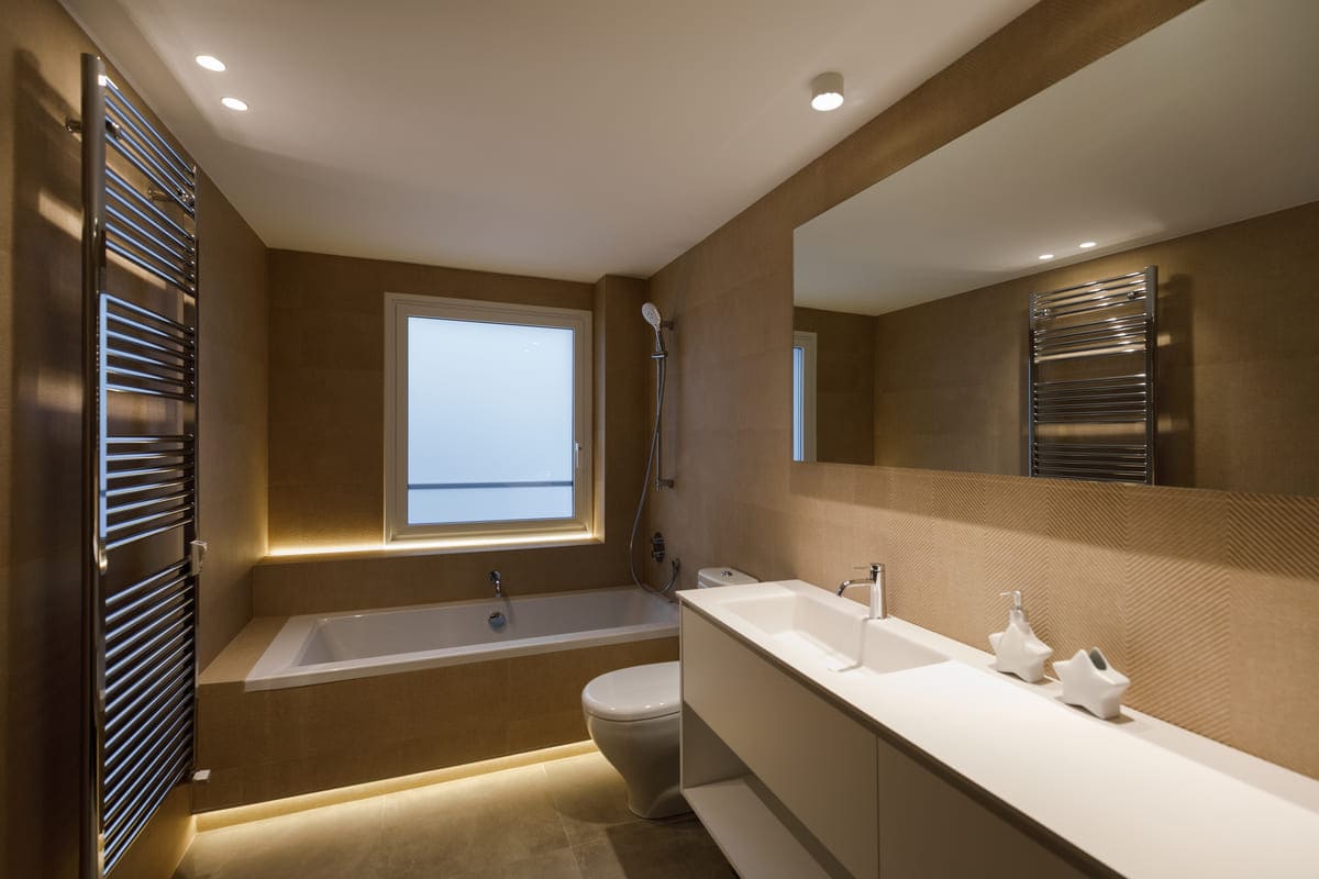 Baño con bañera en tonos tierra y luz indirecta, proyecto GV 26