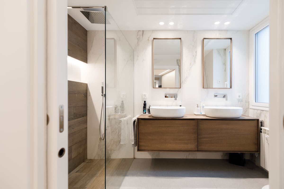 Baño con dos lavabos sobre mueble de madera y mármol blanco