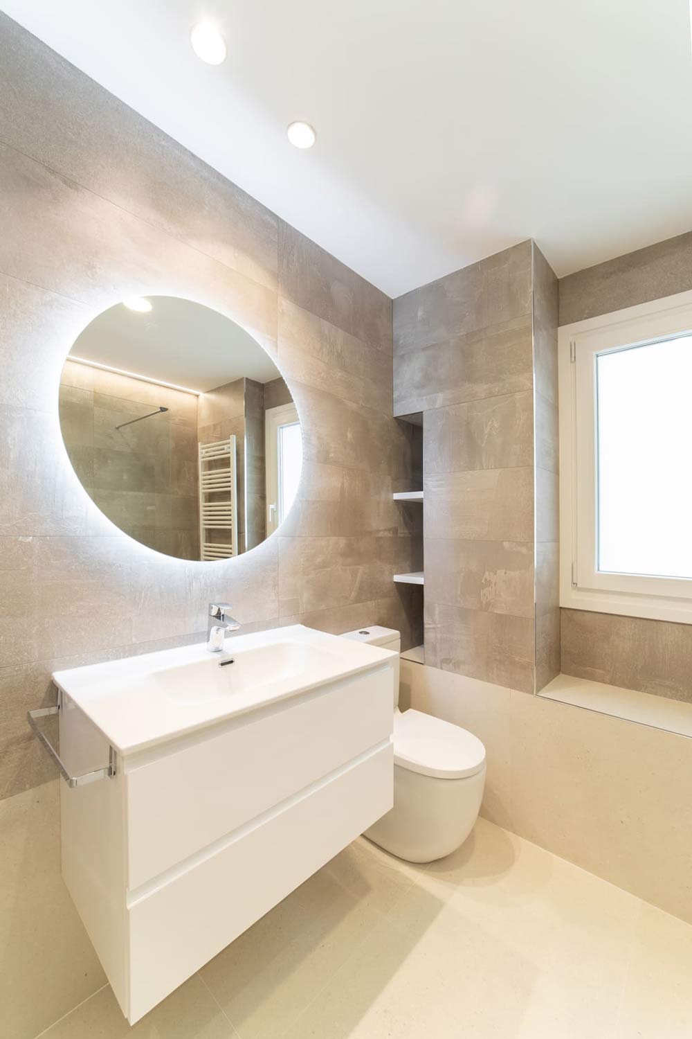 Baño con espejo redondo y mueble blanco suspendido