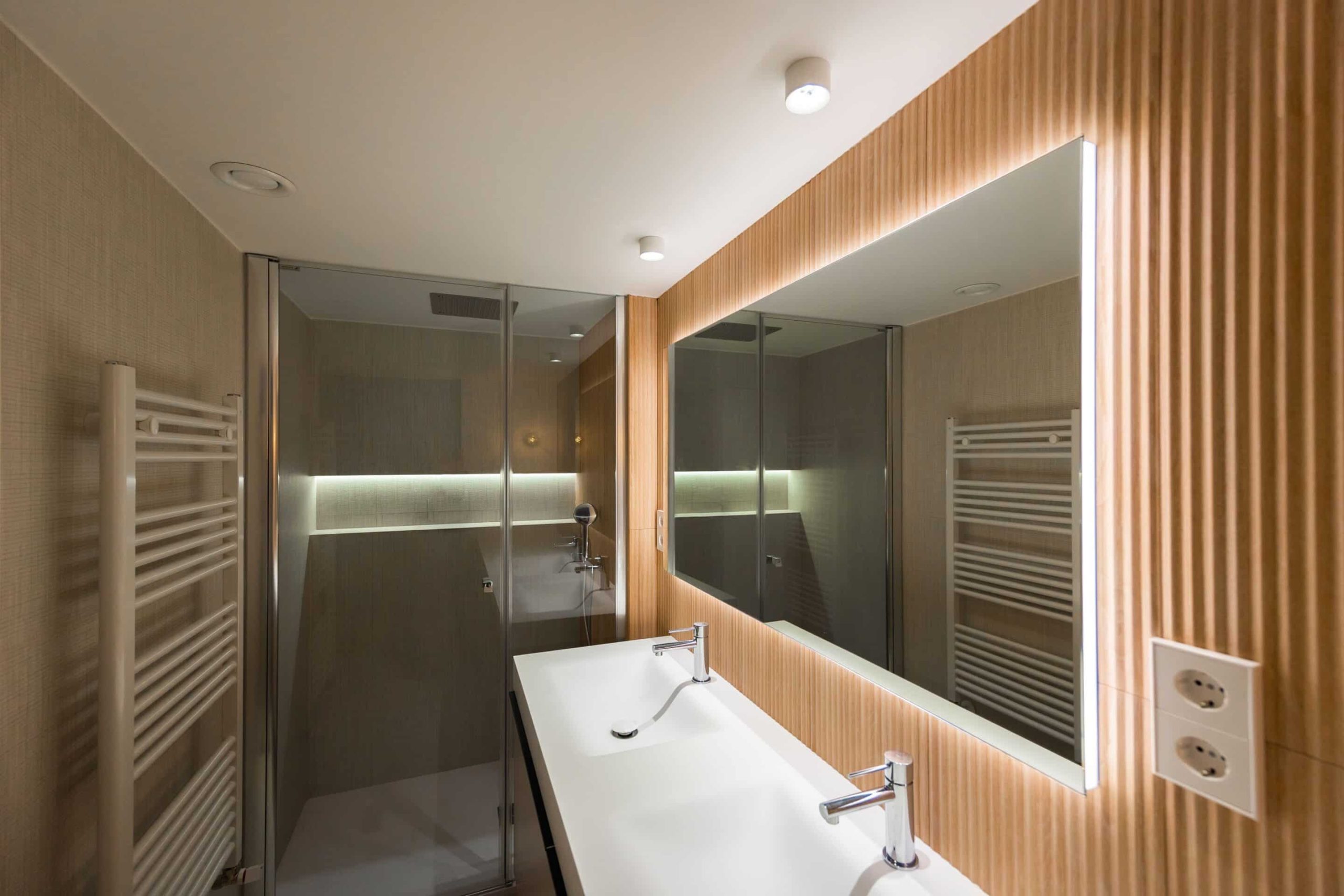 Baño con pared de listones de madera y espejo iluminado