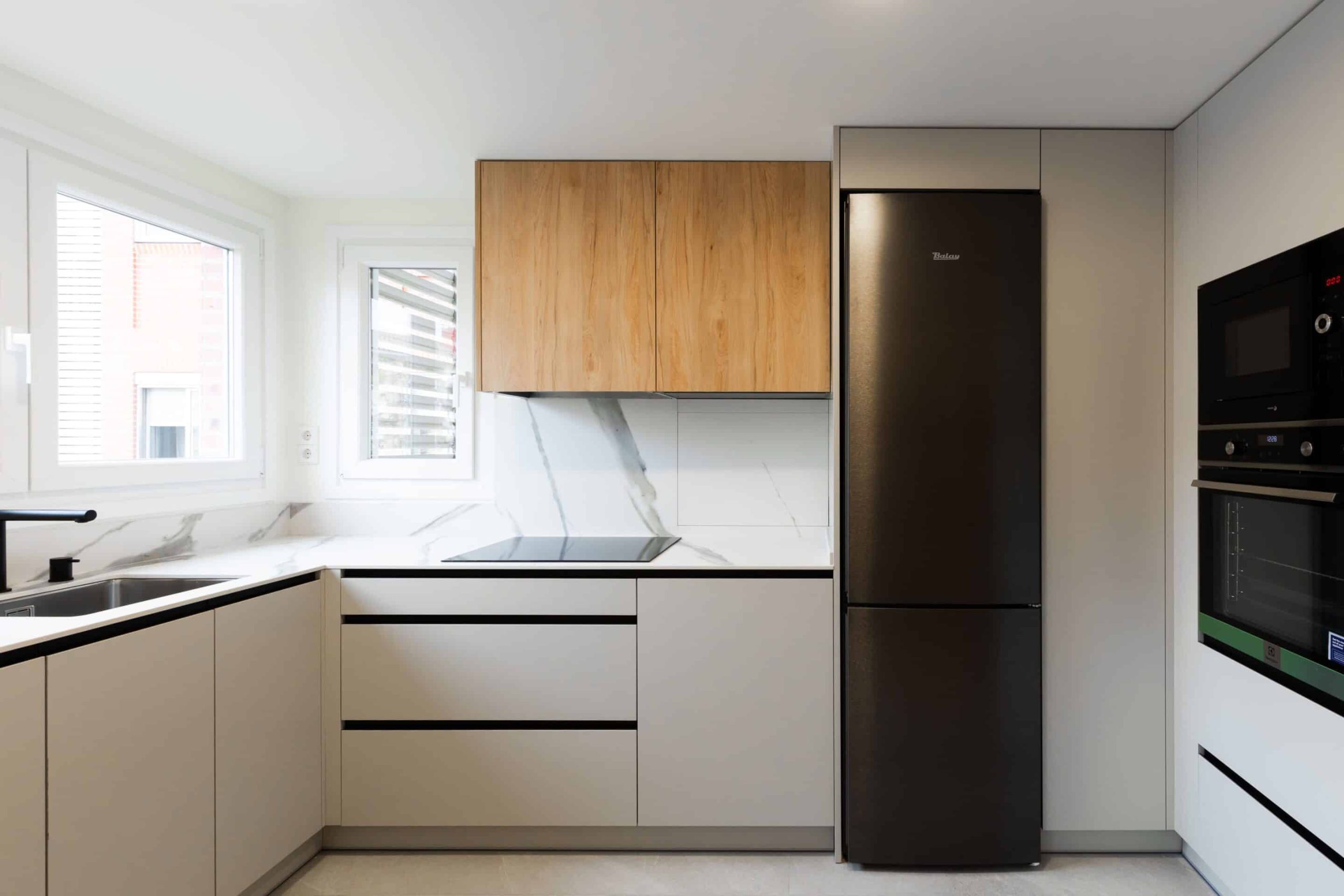 Cocina blanca con altillos de madera y frigorífico negro