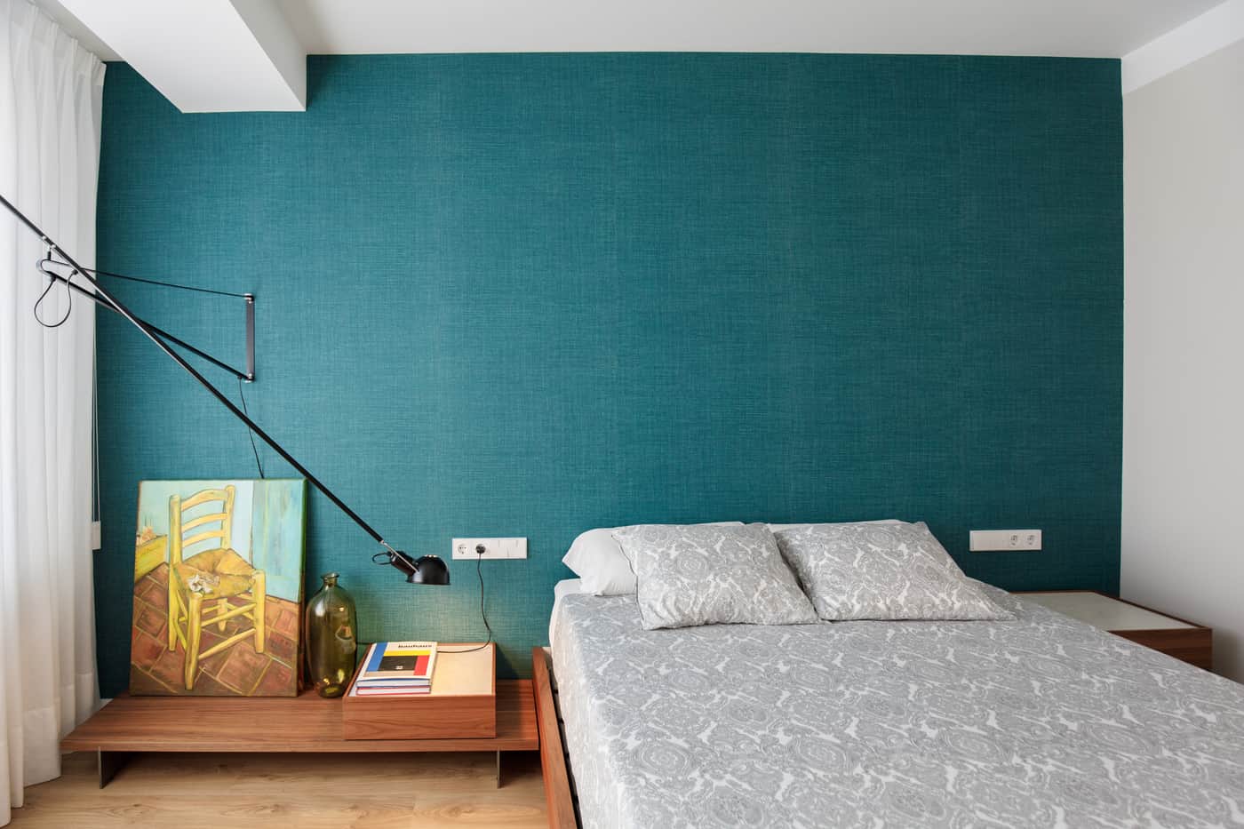 Dormitorio con pared verde azulado y aplique articulado en un piso reformado