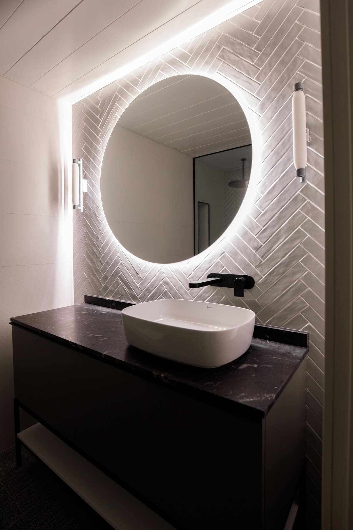 Lavabo con espejo redondo iluminado y mueble negro