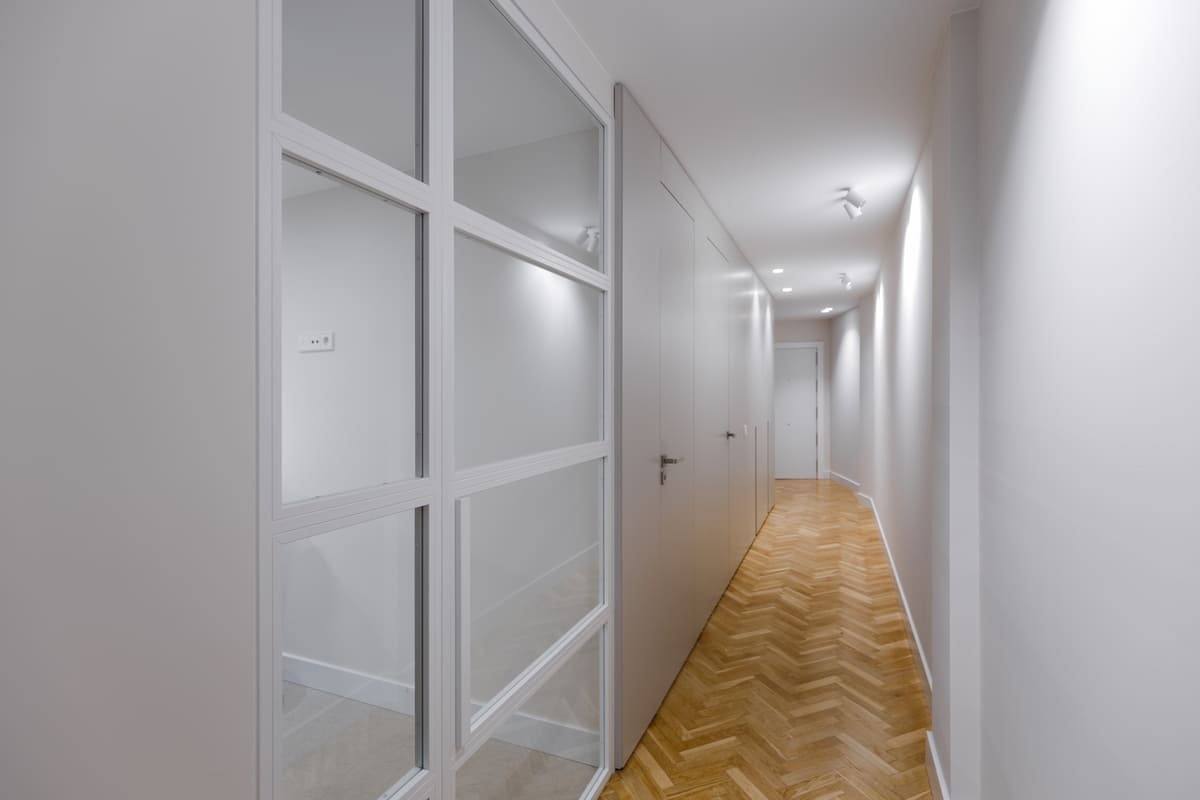 Pasillo con parquet en espiga y puerta acristalada en una vivienda reformada
