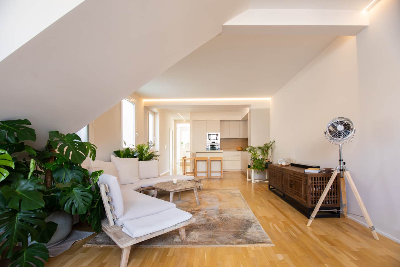 Salón abuhardillado con plantas y sofá blanco en una vivienda reformada