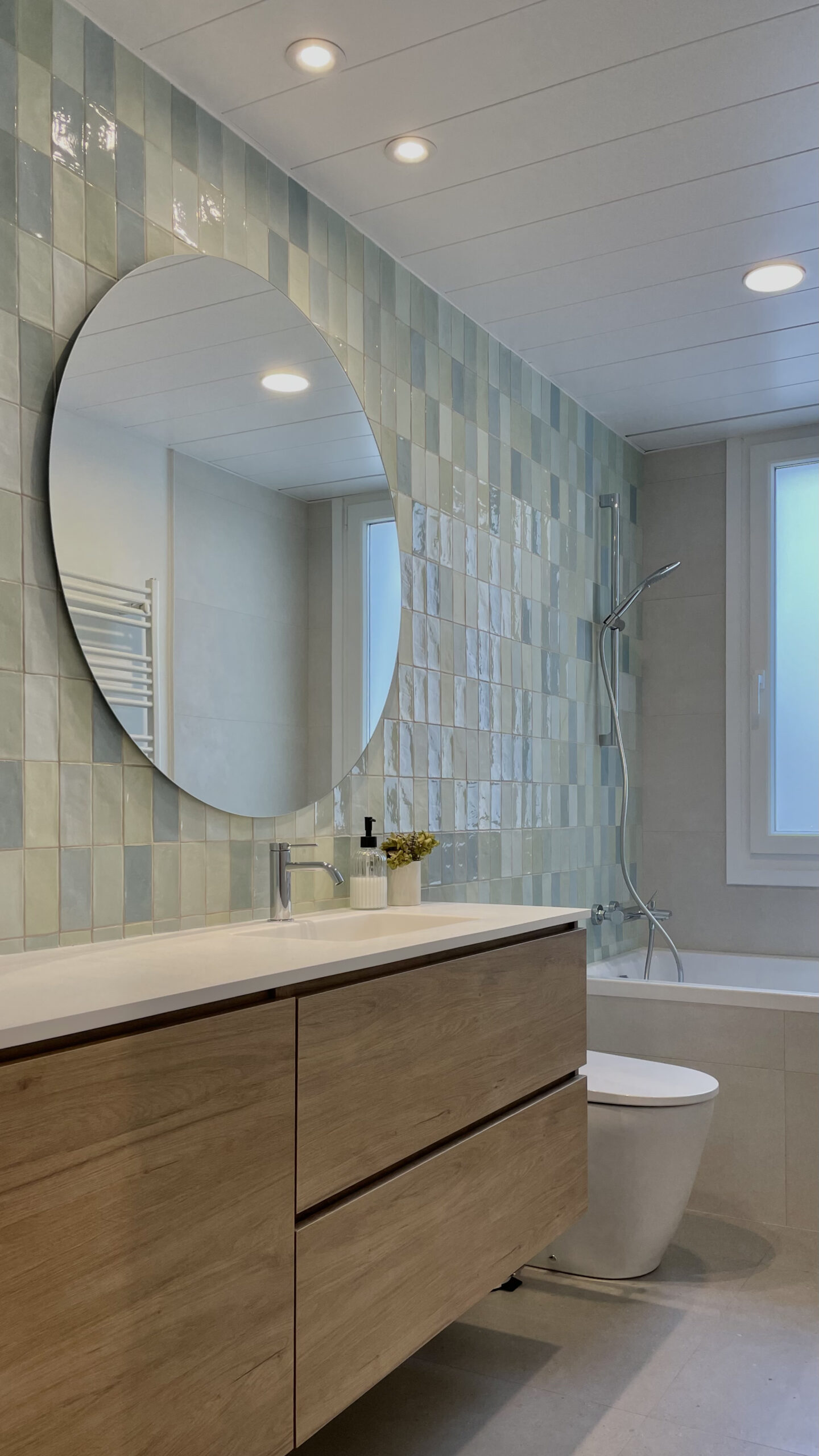 Baño con azulejo verde, espejo redondo y bañera