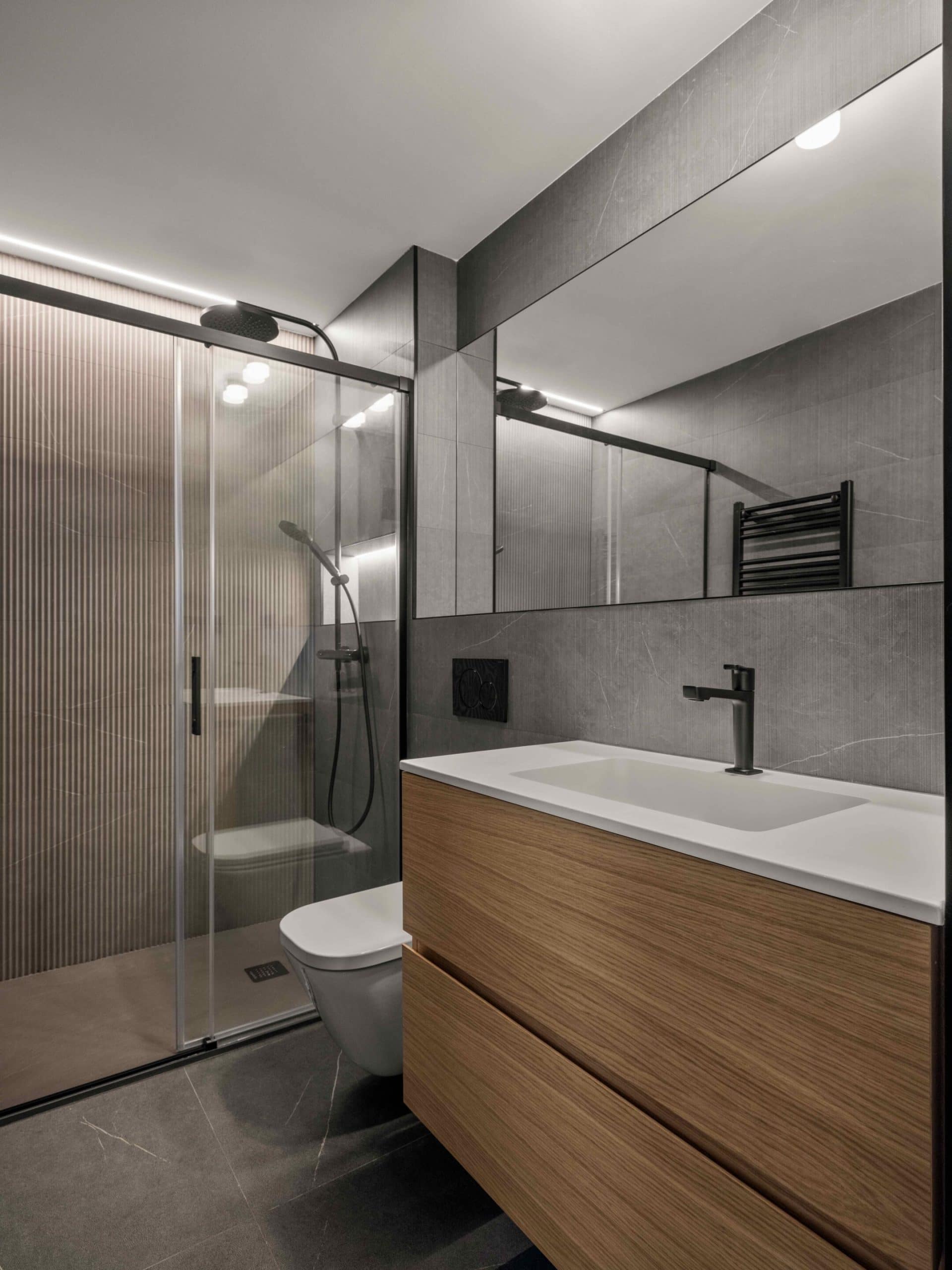 Baño gris reformado con ducha y mueble de madera