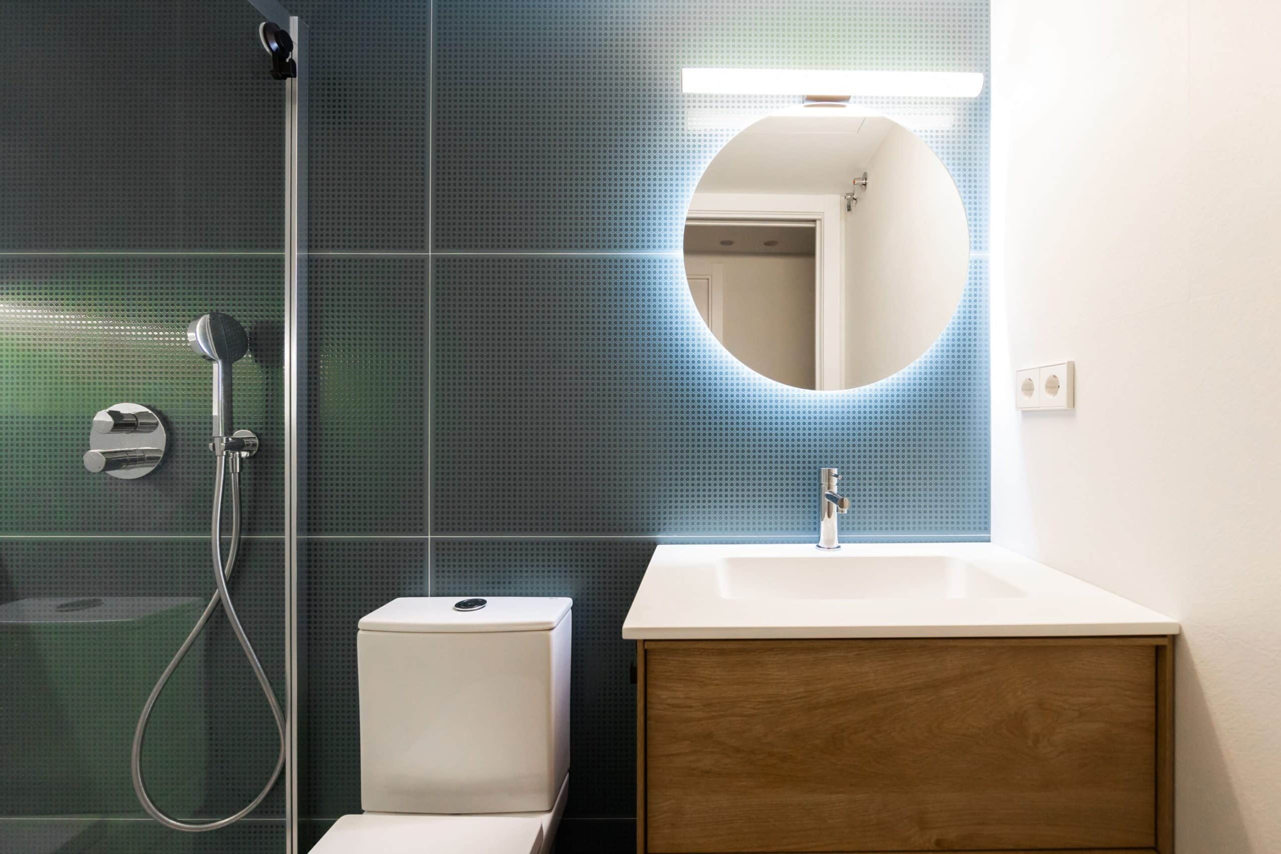 Baño reformado con azulejo verde oscuro y espejo redondo
