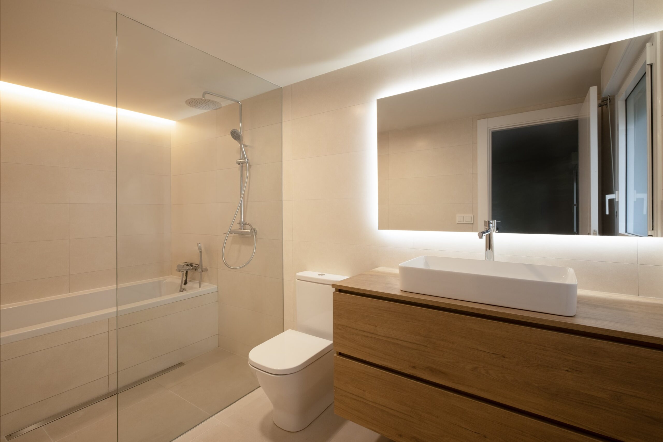 Baño con bañera, mampara y espejo iluminado en una casa reformada
