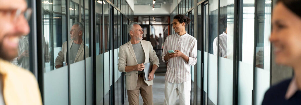 personas caminando y charlando en pasillo de oficina moderna con paredes de cristal y ambiente laboral relajado