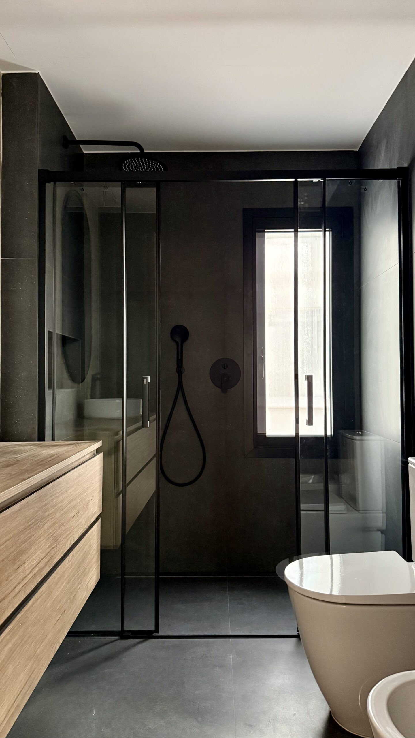 Baño con mampara negra y suelo oscuro