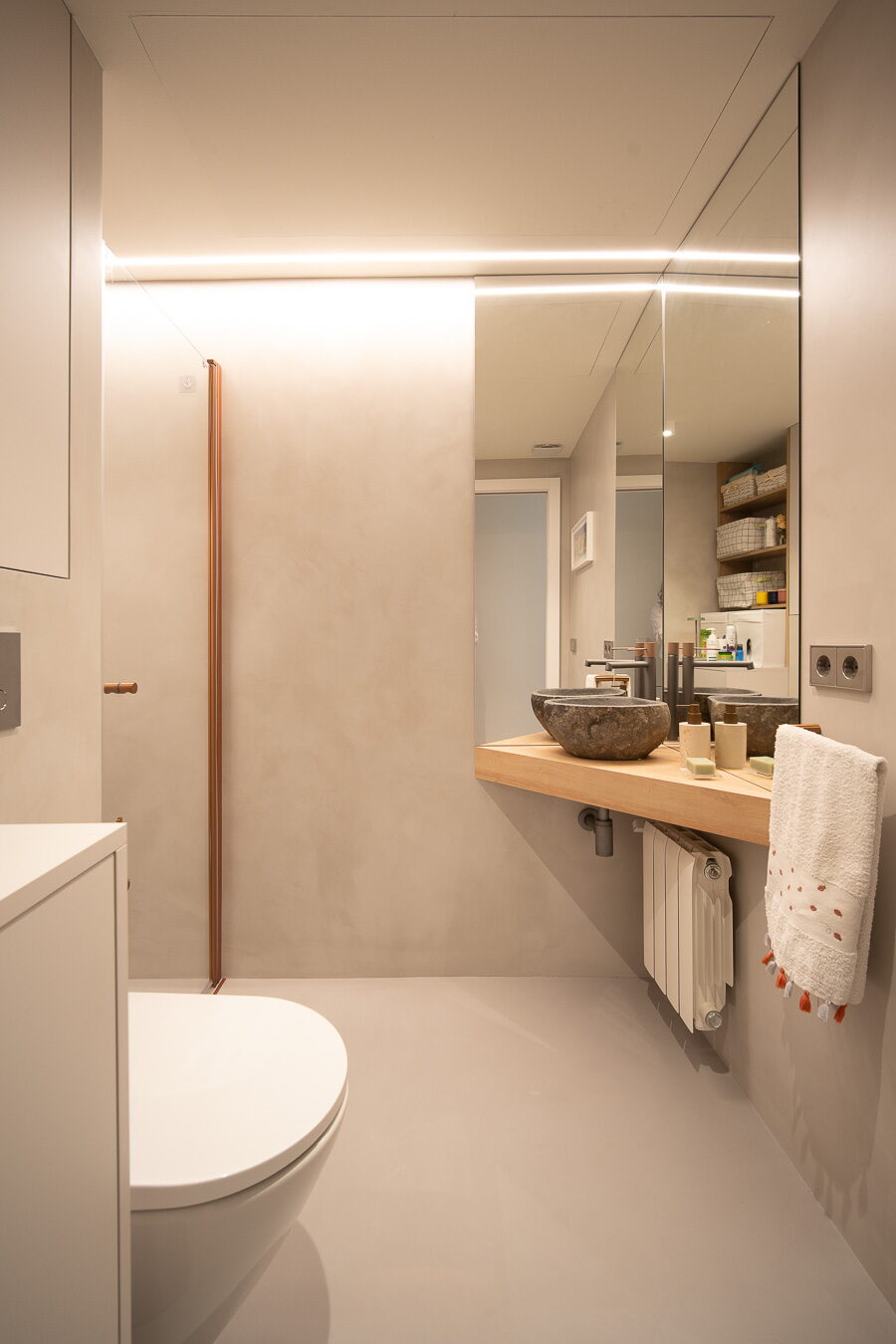 Baño con acabados continuos y lavabo de piedra tras la reforma