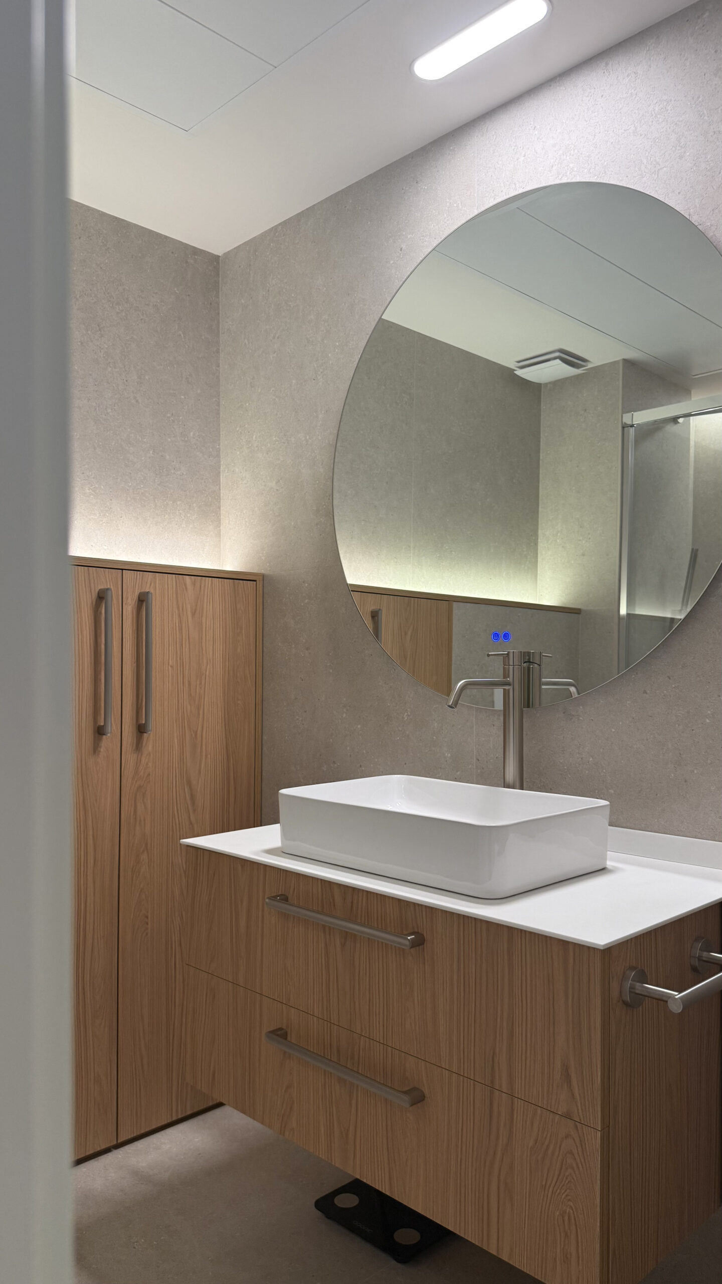 Baño con mueble de madera, lavabo sobre encimera y espejo redondo