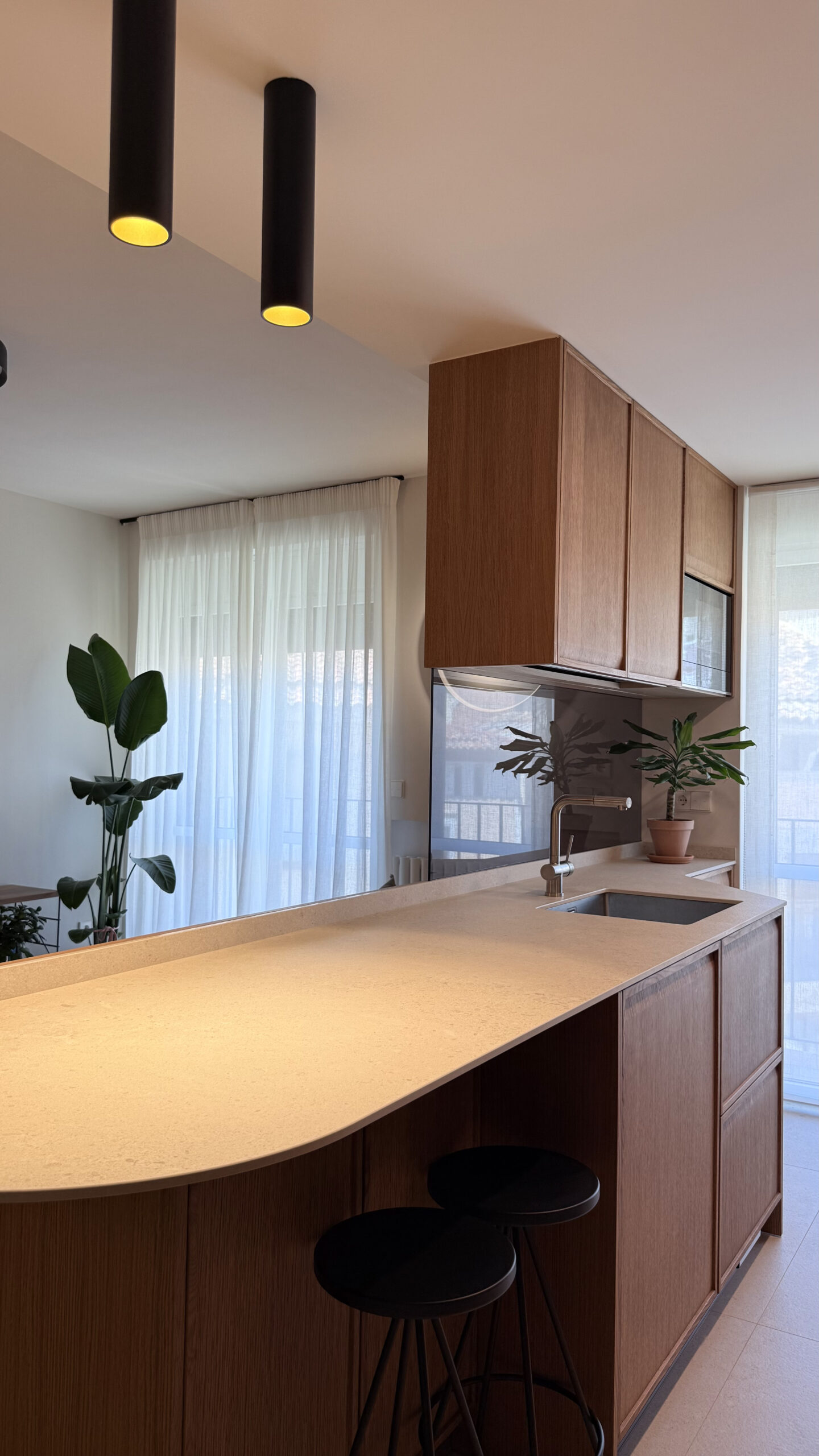 Isla de cocina con extremo curvo y taburetes negros en un piso reformado