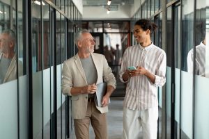 personas caminando y charlando en pasillo de oficina moderna con paredes de cristal y ambiente laboral relajado