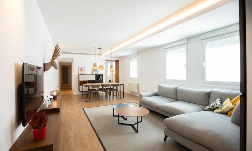 Salón amplio con sofá gris y comedor al fondo